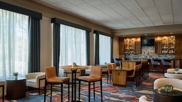 Un vestíbulo de hotel con una zona de bar, arreglos de asientos y un amplio ventanal con cortinas.