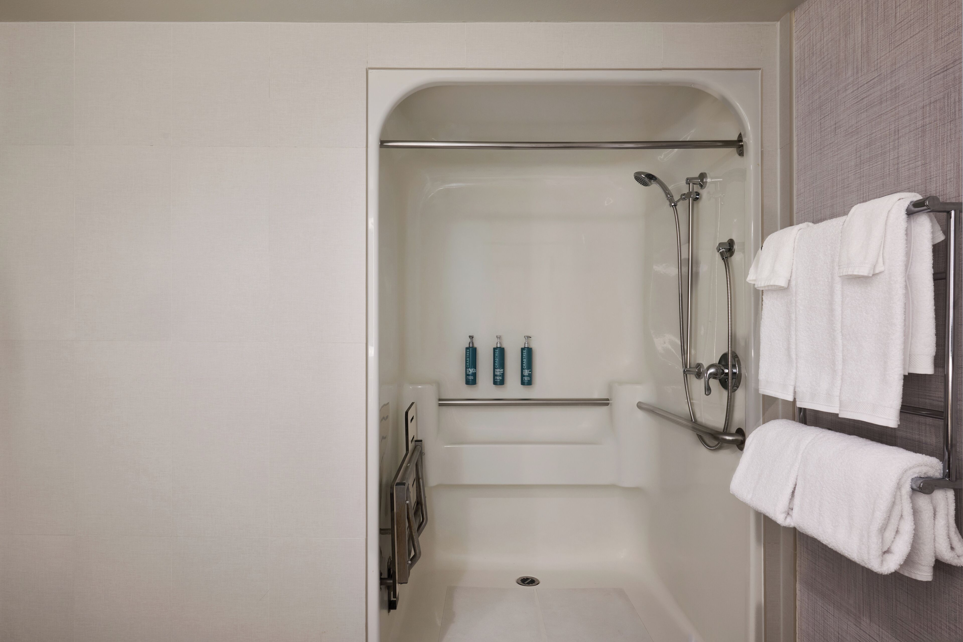 A modern bathroom with a walk-in shower, a glass-enclosed toilet, and a towel rack with towels.