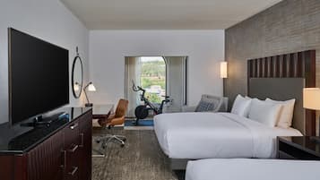 Habitación de hotel con televisión, bicicleta estática, dos camas, escritorio y vistas a zonas verdes.