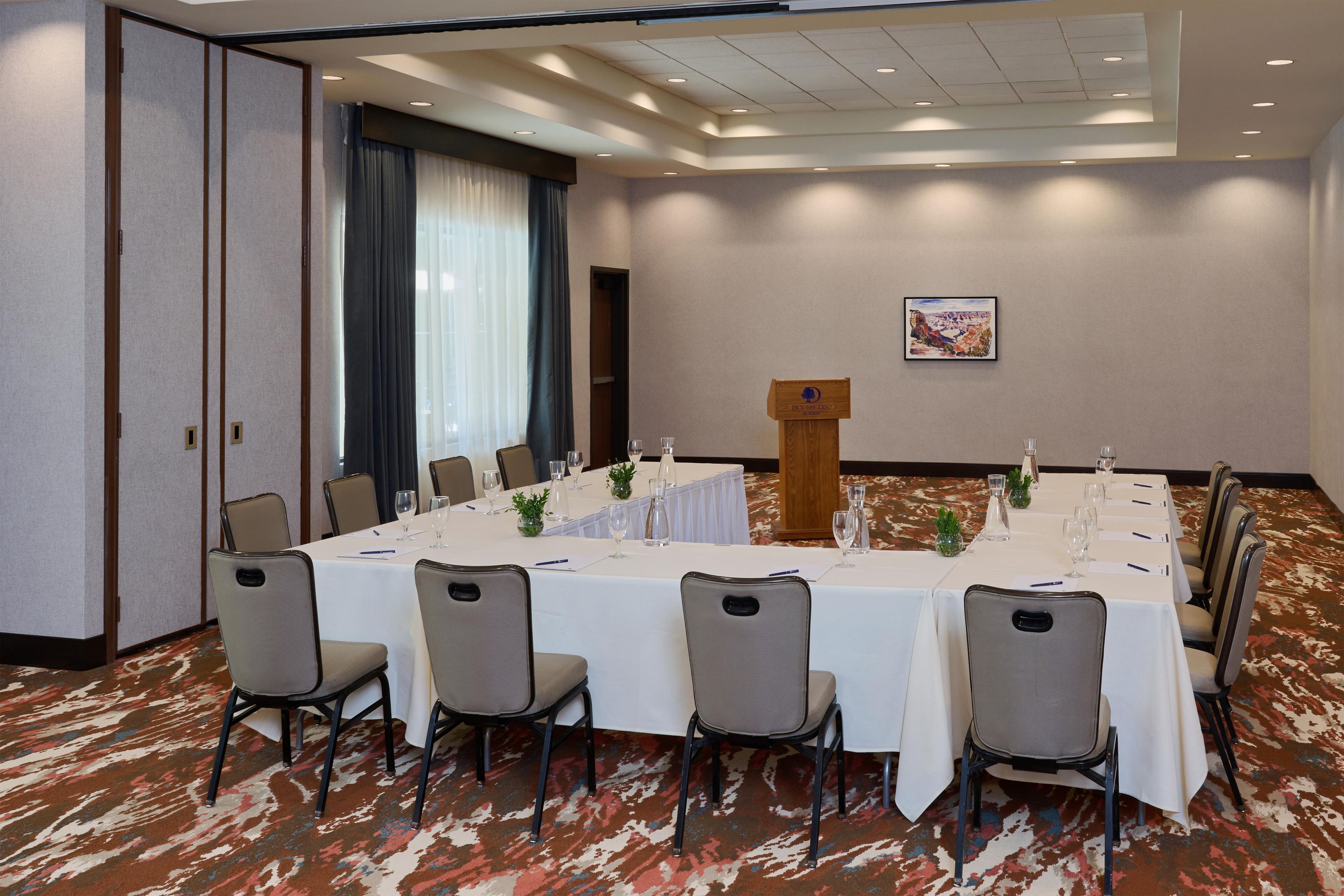 Ein Konferenzraum mit einem langen Tisch, Stühlen, einem Rednerpult und einem gerahmten Bild an der Wand.