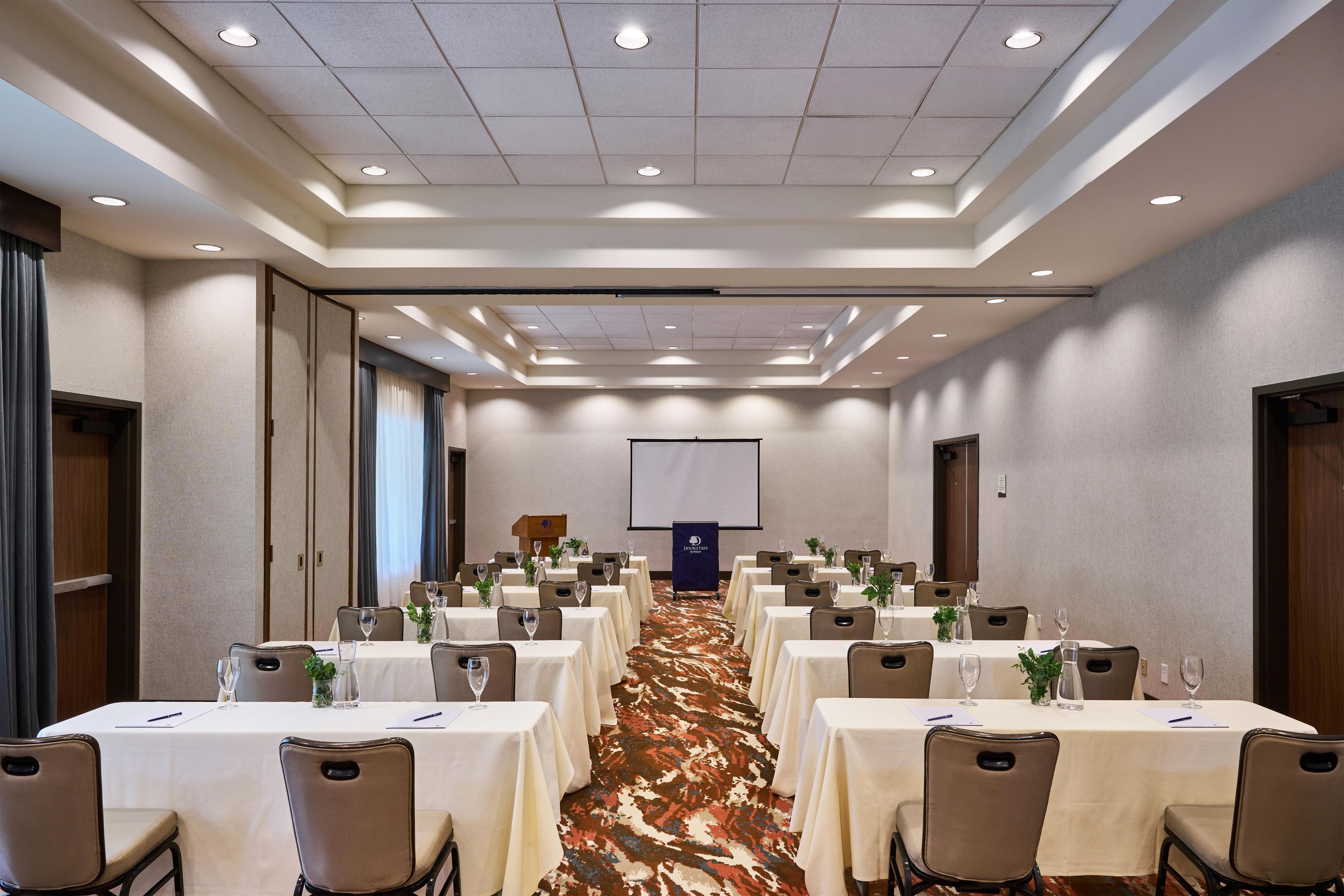 Een congreszaal met meerdere tafels, stoelen en een spreekgestoelte vooraan.