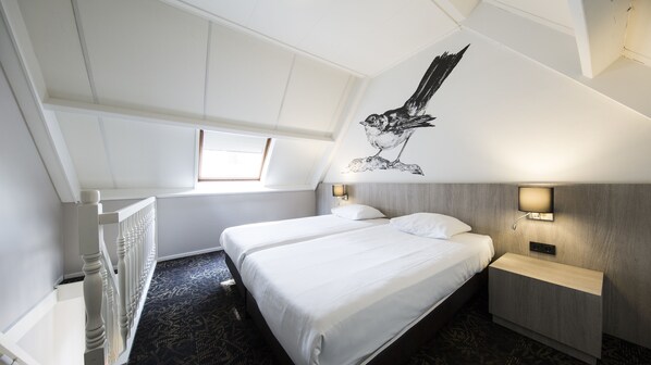 A modern hotel room with a sloped ceiling, two single beds, a small bedside table with a lamp, a wall-mounted TV, and a large window providing natural light. - Fletcher Hotel-Restaurant De Broeierd (Enschede)