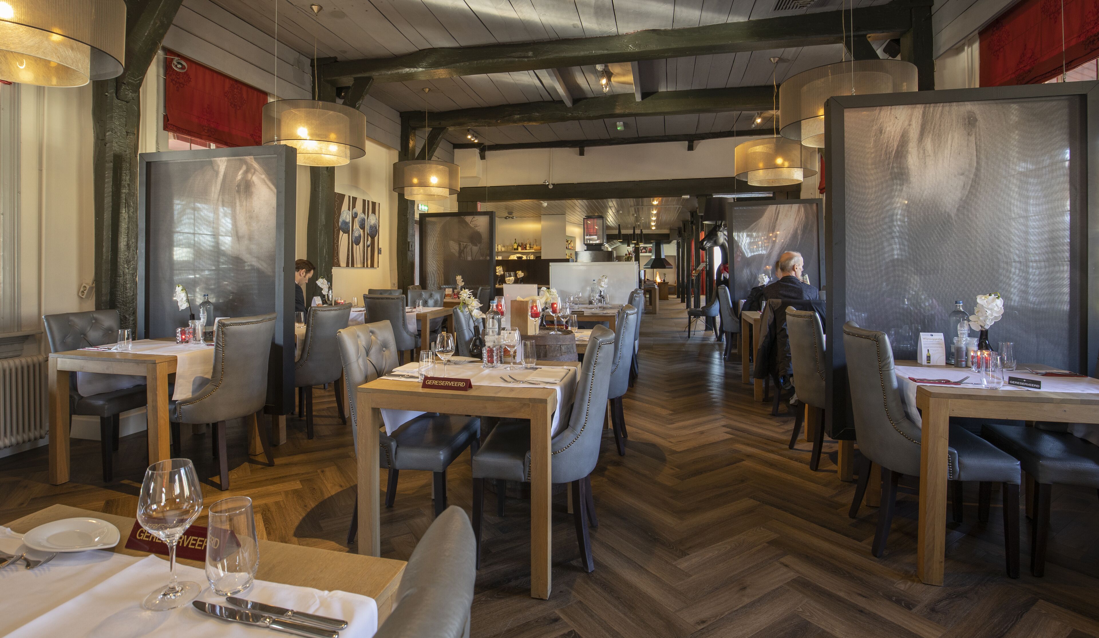 Ein Restaurant mit Holztischen und -stühlen, einem Fischgrätparkett und hängenden Pendelleuchten.