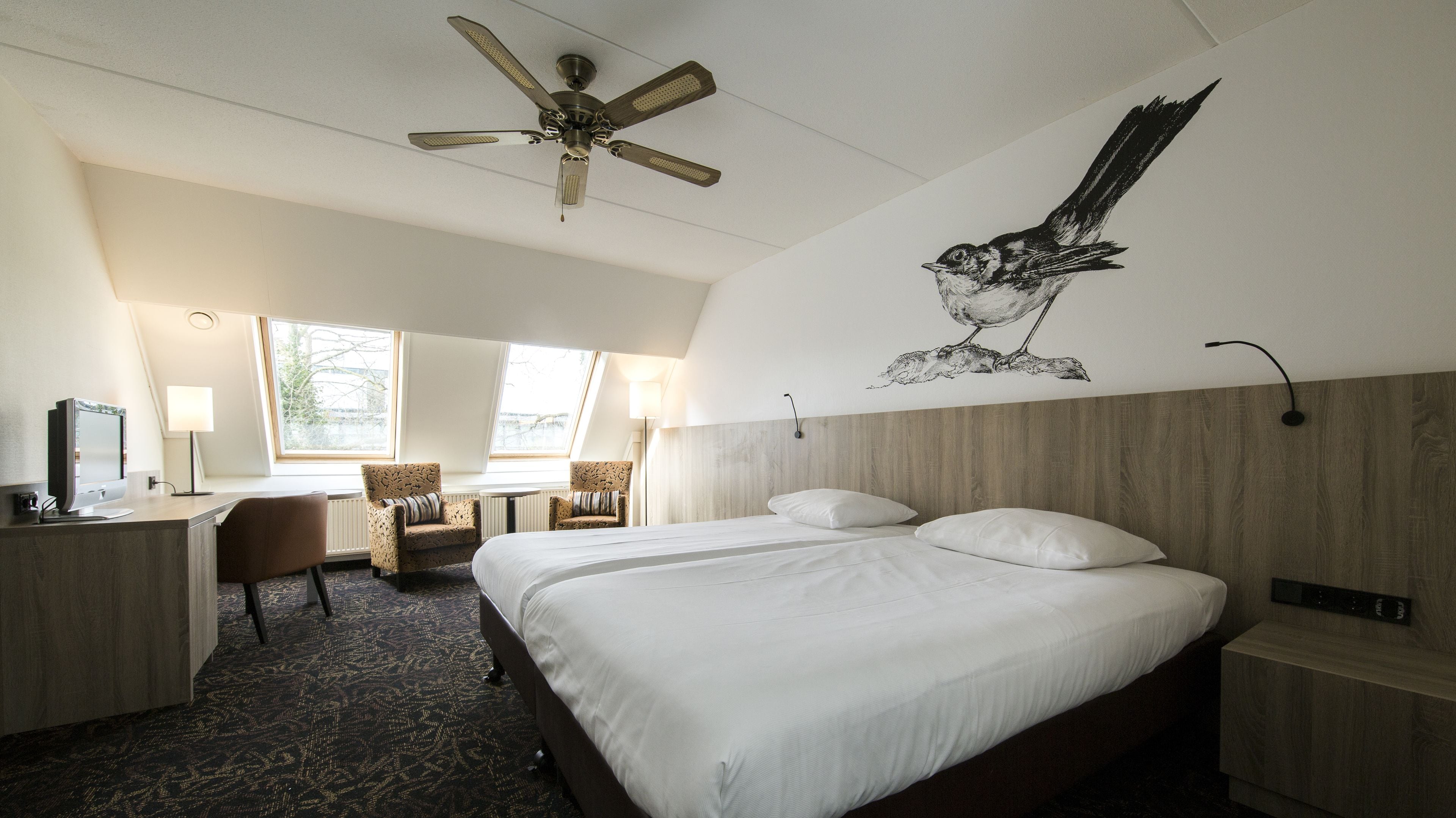 Une chambre d’hôtel équipée d’un lit, d’un bureau, d’une chaise et d’un ventilateur de plafond.
