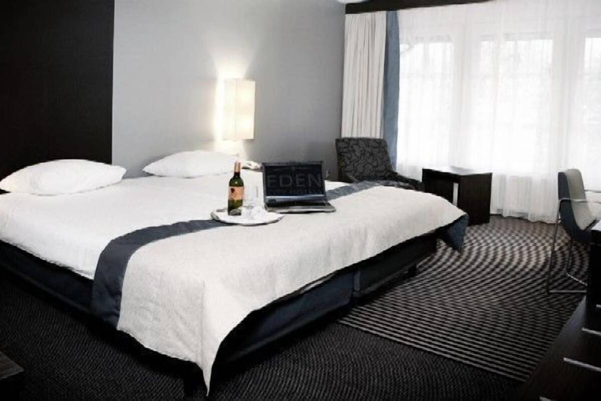 Ein Hotelzimmer mit einem großen Bett, zwei Nachttischen, einem Schreibtisch und einem Sessel.