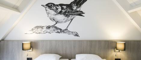 Habitación de hotel con cama, dos lámparas de noche y un adhesivo de pájaro en la pared.