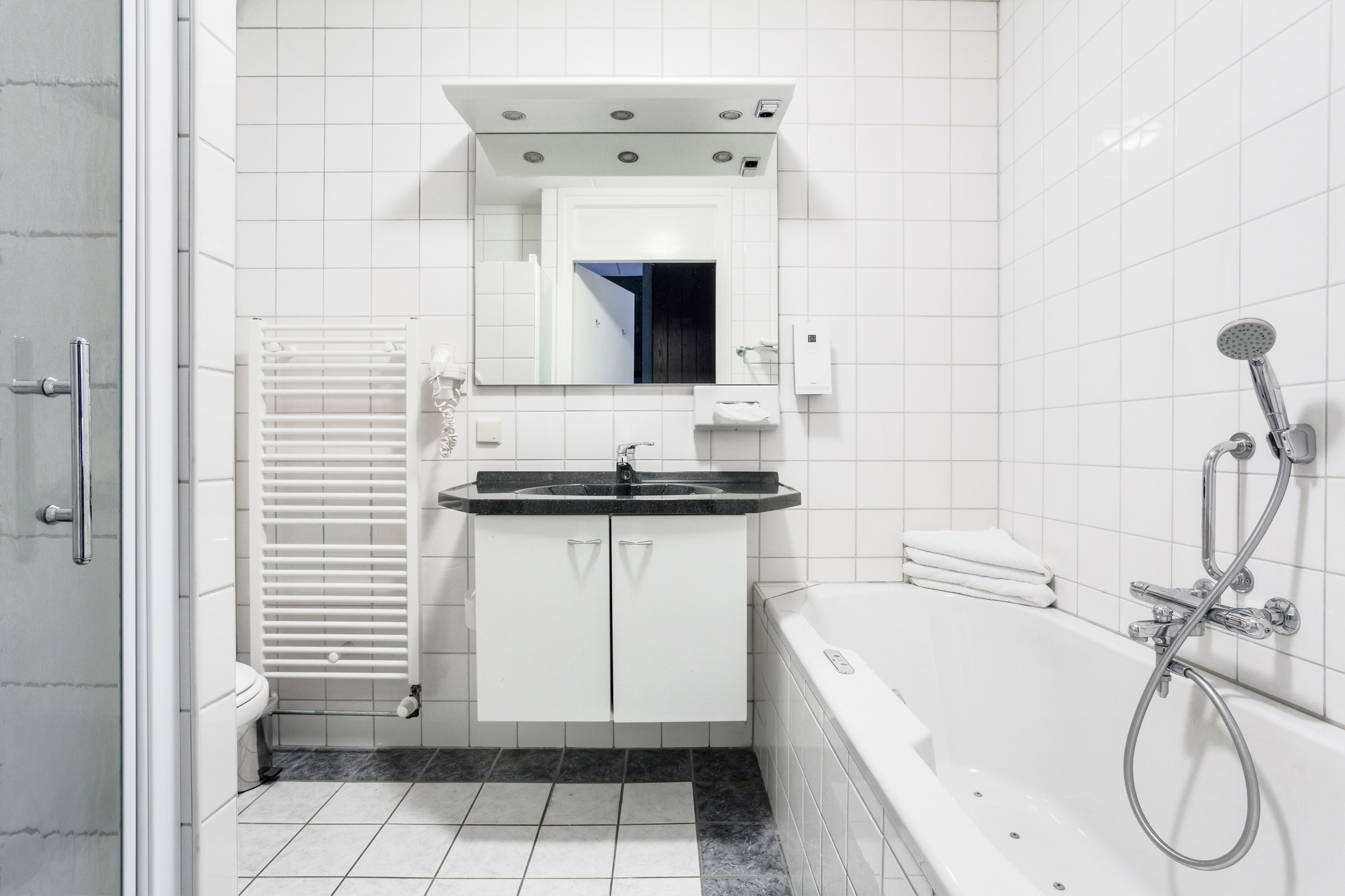 Een moderne badkamer met een witte wastafel, een spiegel erboven, een wit toilet, een witte badkuip en een douche.
