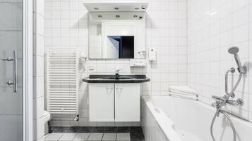 Een moderne badkamer met een witte wastafel, een spiegel erboven, een wit toilet, een witte badkuip en een douche.
