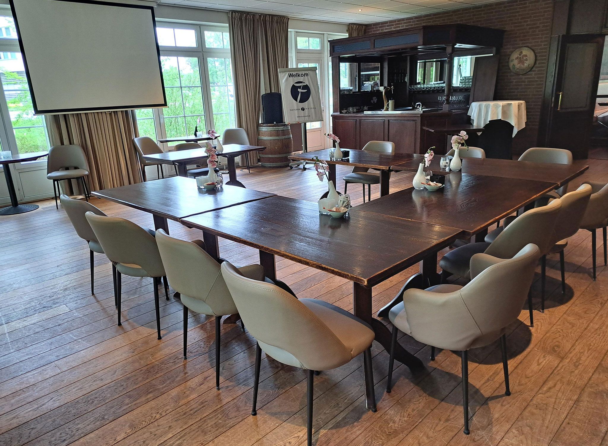 A conference room with a large table, chairs, a projector screen, and a bar area with bottles.