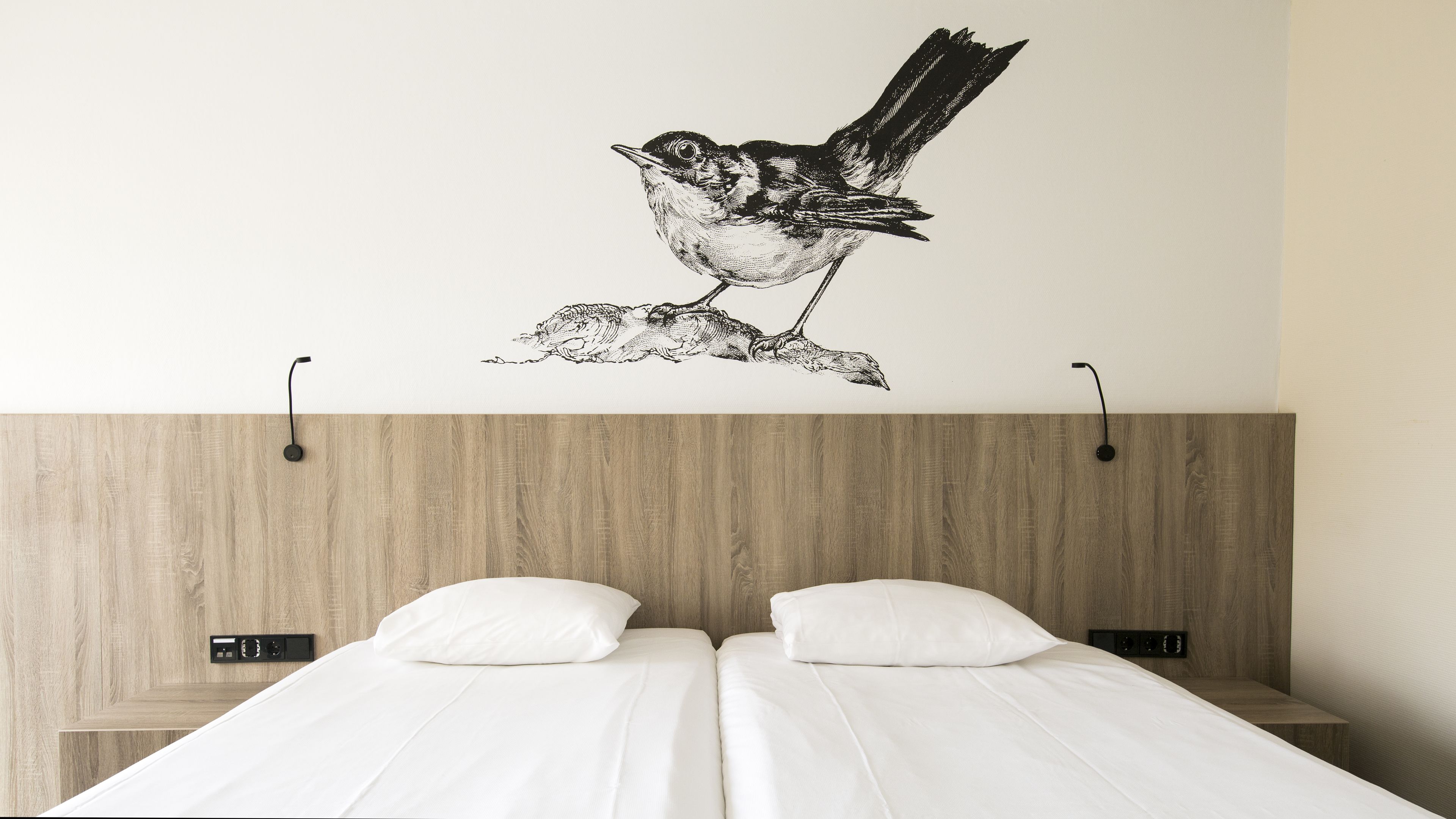 Un dormitorio con una cama, dos mesitas de noche, un aplique de pared y un vinilo decorativo de un pájaro.