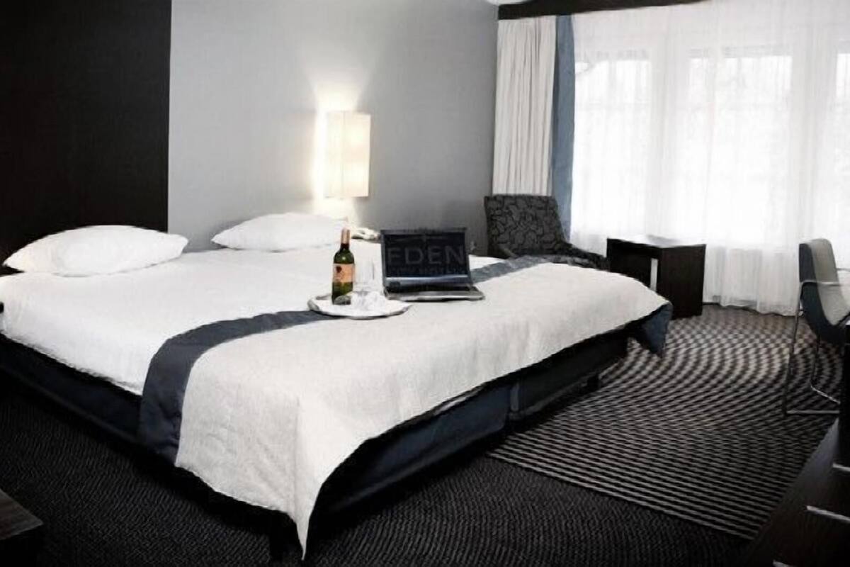Ein Hotelzimmer mit Bett, Laptop, einer Weinflasche und einem Sessel.