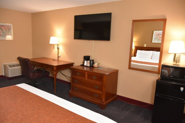 A hotel room with a bed, desk, chair, dresser, television, and a mirror.