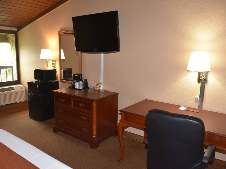 Hotellihuone, jossa on sänky, puinen työpöytä, televisio, lipasto ja kaksi seinälle asennettua lamppua.
