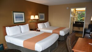 Une chambre d’hôtel avec deux lits, un bureau, une chaise et une salle de bain visible à travers une porte ouverte.