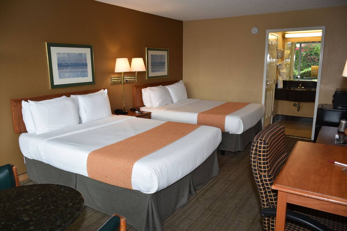 Une chambre d’hôtel avec deux lits, un bureau, une chaise et une salle de bain visible à travers une porte ouverte.