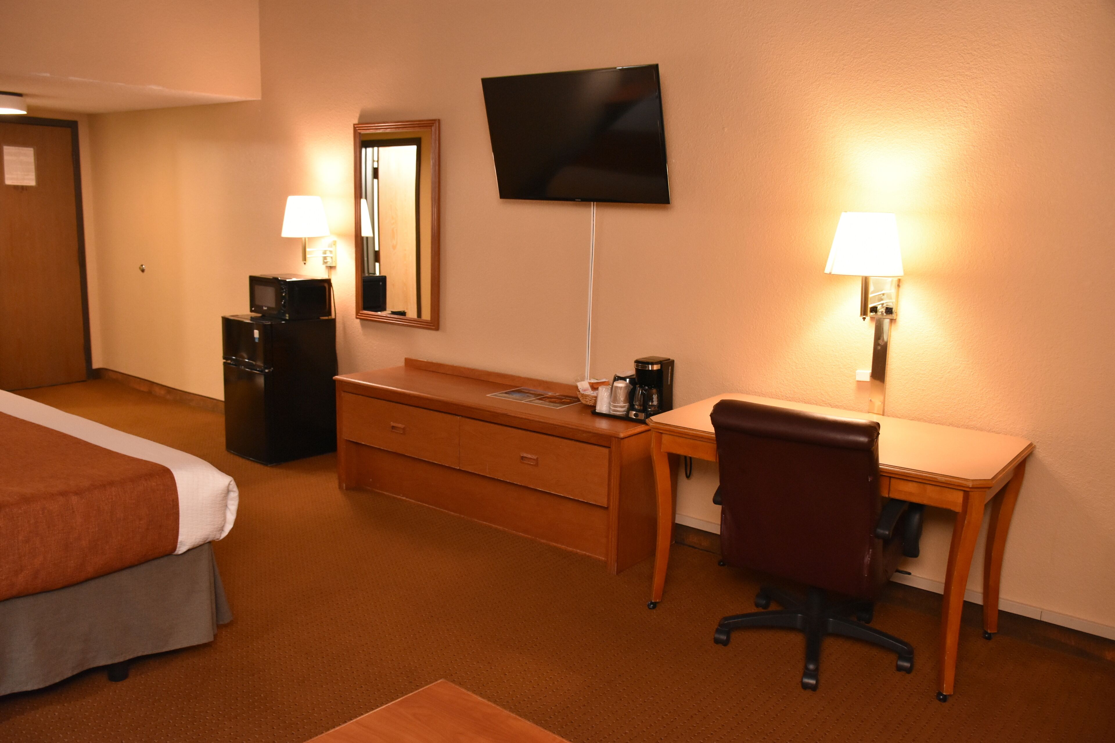 Une chambre d’hôtel équipée d’un lit, d’un bureau, d’une chaise, d’une télévision, d’un miroir et d’une lampe.