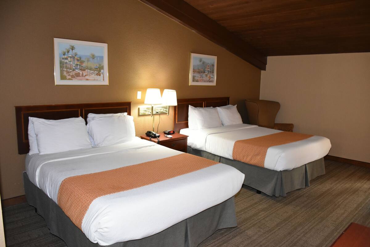 A hotel room with two beds, a nightstand with a lamp, and framed pictures on the wall.