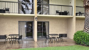Un immeuble de deux étages doté d’un balcon à l’étage supérieur, et offrant un espace extérieur aménagé avec des tables et des chaises.