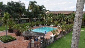 Un espace piscine avec des chaises longues, un coin salon abrité et des palmiers.