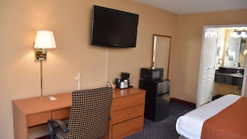 A hotel room with a bed, a desk with a chair, a television, a microwave, a refrigerator, a coffee maker, and a mirror.