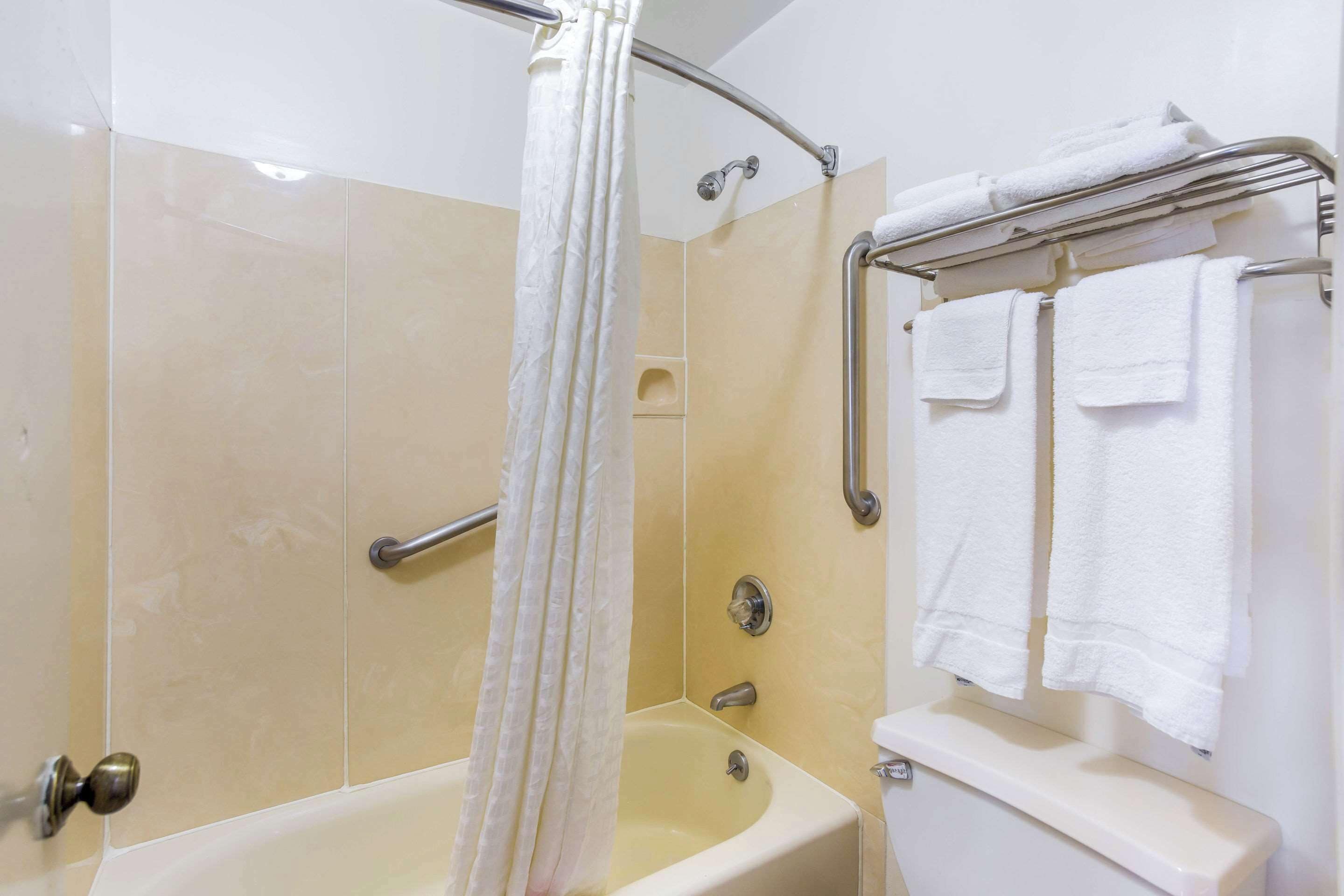 A bathroom with a bathtub, a shower curtain, a towel rack with towels, and a toilet.