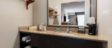 A hotel bathroom with a granite countertop, a sink, a mirror, a towel rack, and a coffee maker.
