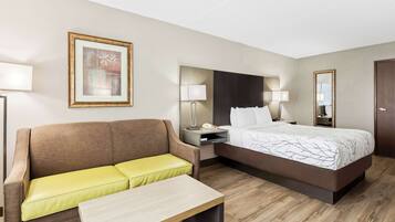 Habitación de hotel con cama, sofá, mesita de noche, lámpara, cuadro enmarco y espejo.