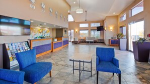 Un vestíbulo de hotel con mostrador de recepción, zona de estar y grandes ventanales.
