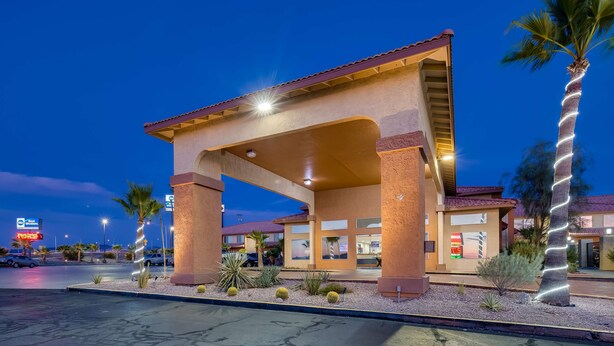 Entrada de hotel con un gran arco, palmeras y un estacionamiento.