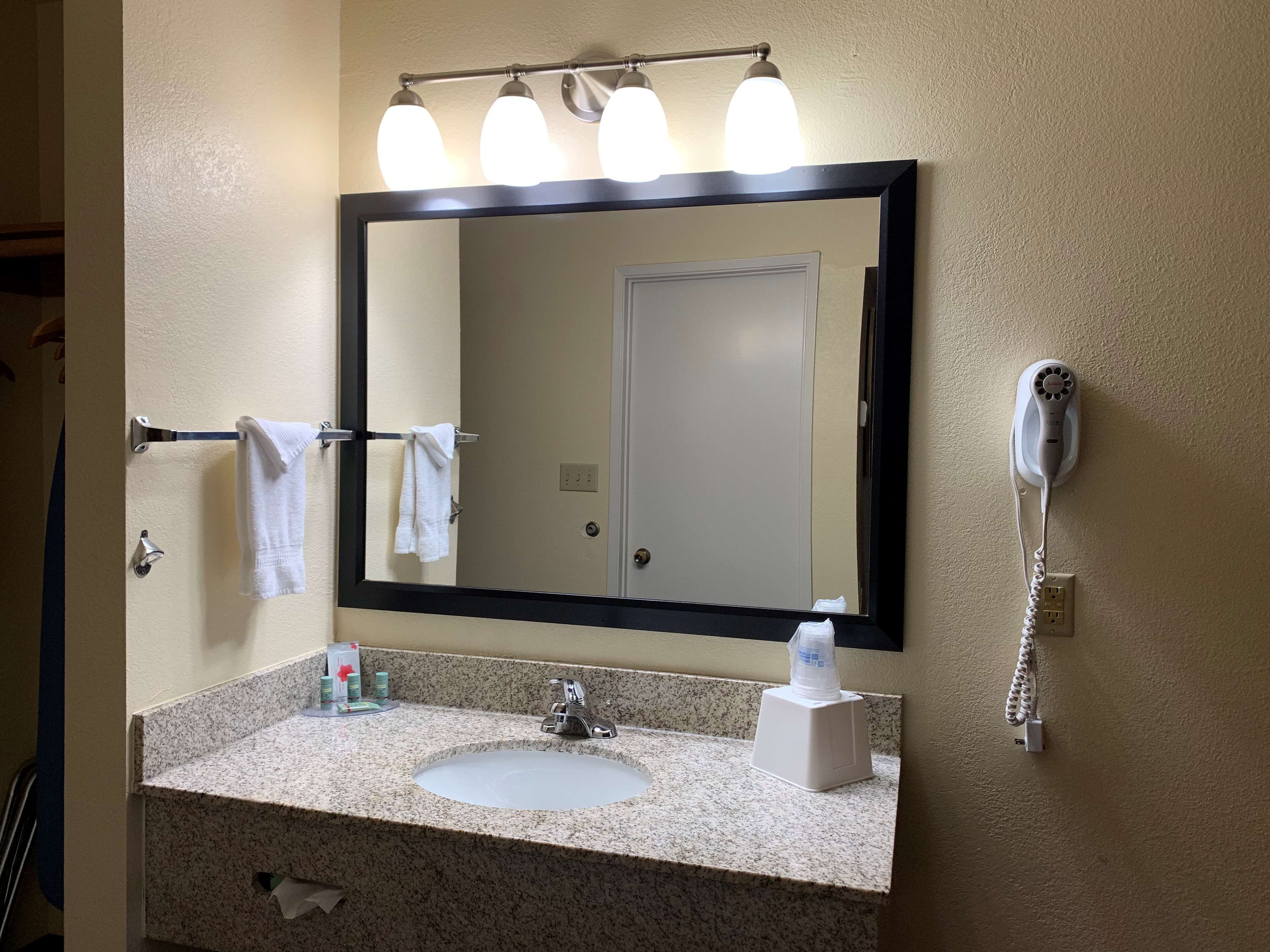 A bathroom with a sink, mirror, towel rack, and a hairdryer on the wall.
