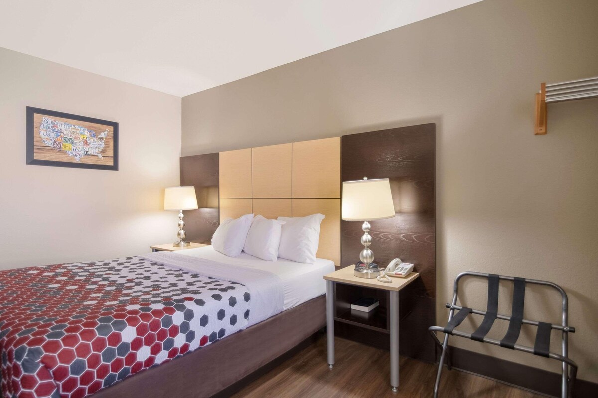 A hotel room with a bed, two bedside tables with lamps, a chair, and a wall map.