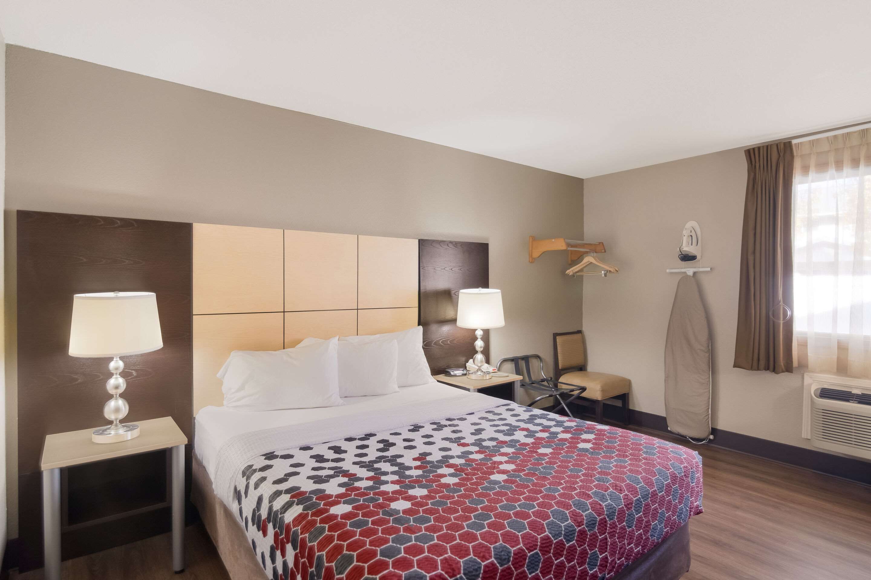 A hotel room with a bed, two bedside lamps, a chair, a desk, and a coat rack.