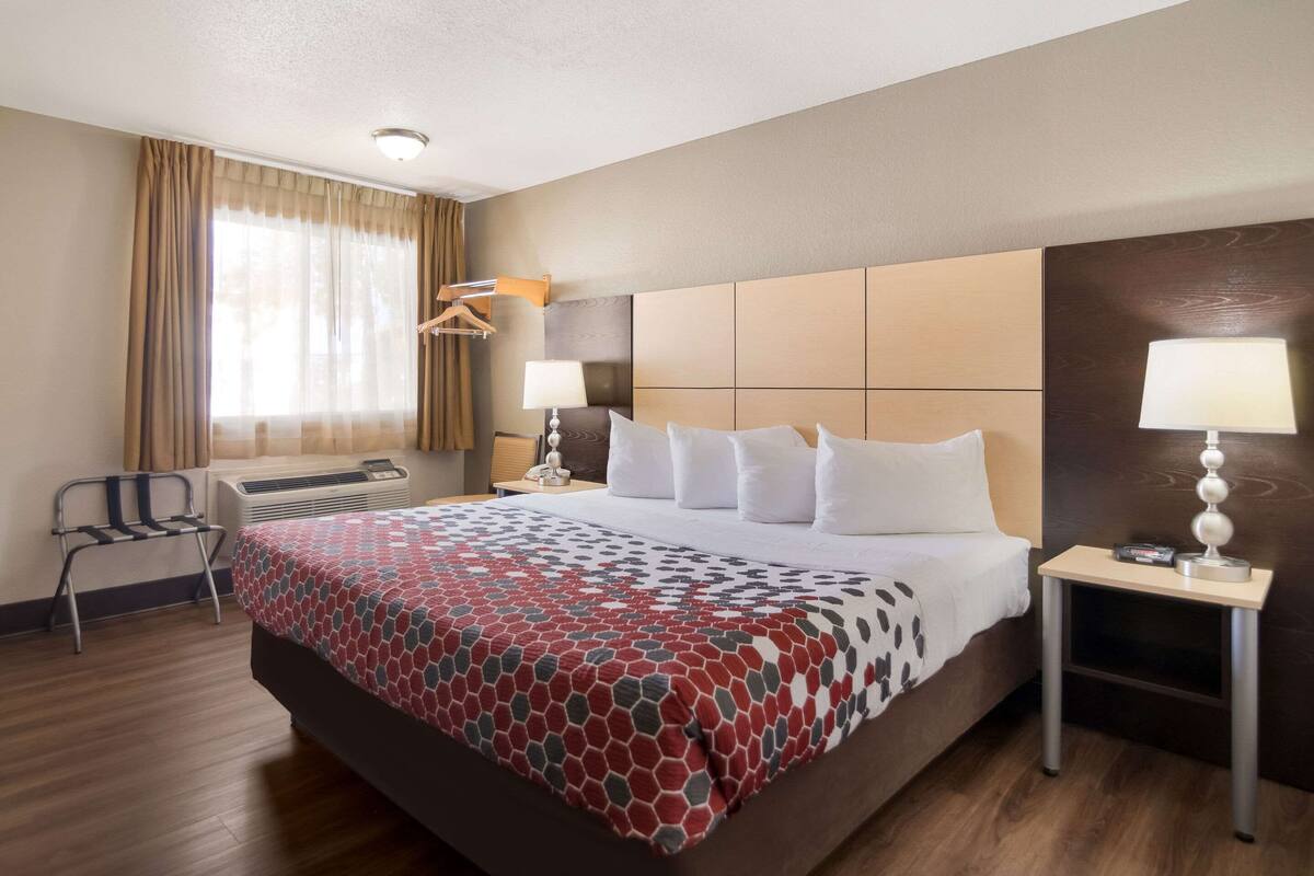 Una habitación de hotel con una cama grande, dos mesitas de noche, una silla, un escritorio y un ventanal con cortinas.