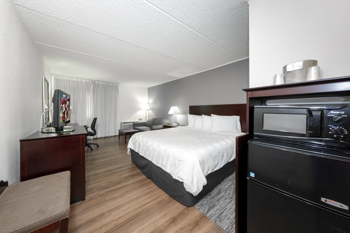 A hotel room with a bed, desk, chair, and a microwave.