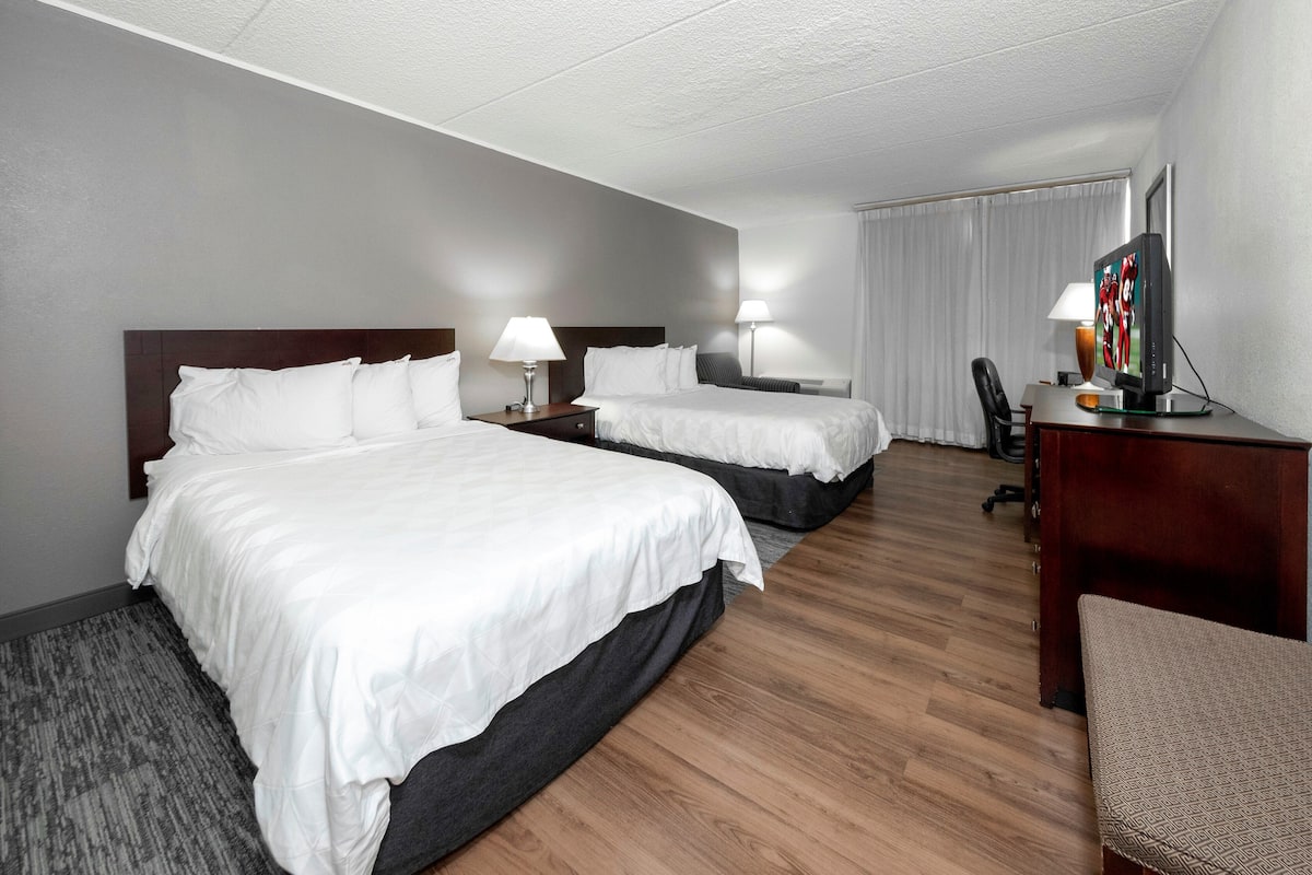A hotel room with two beds, a desk, a chair, and a television.