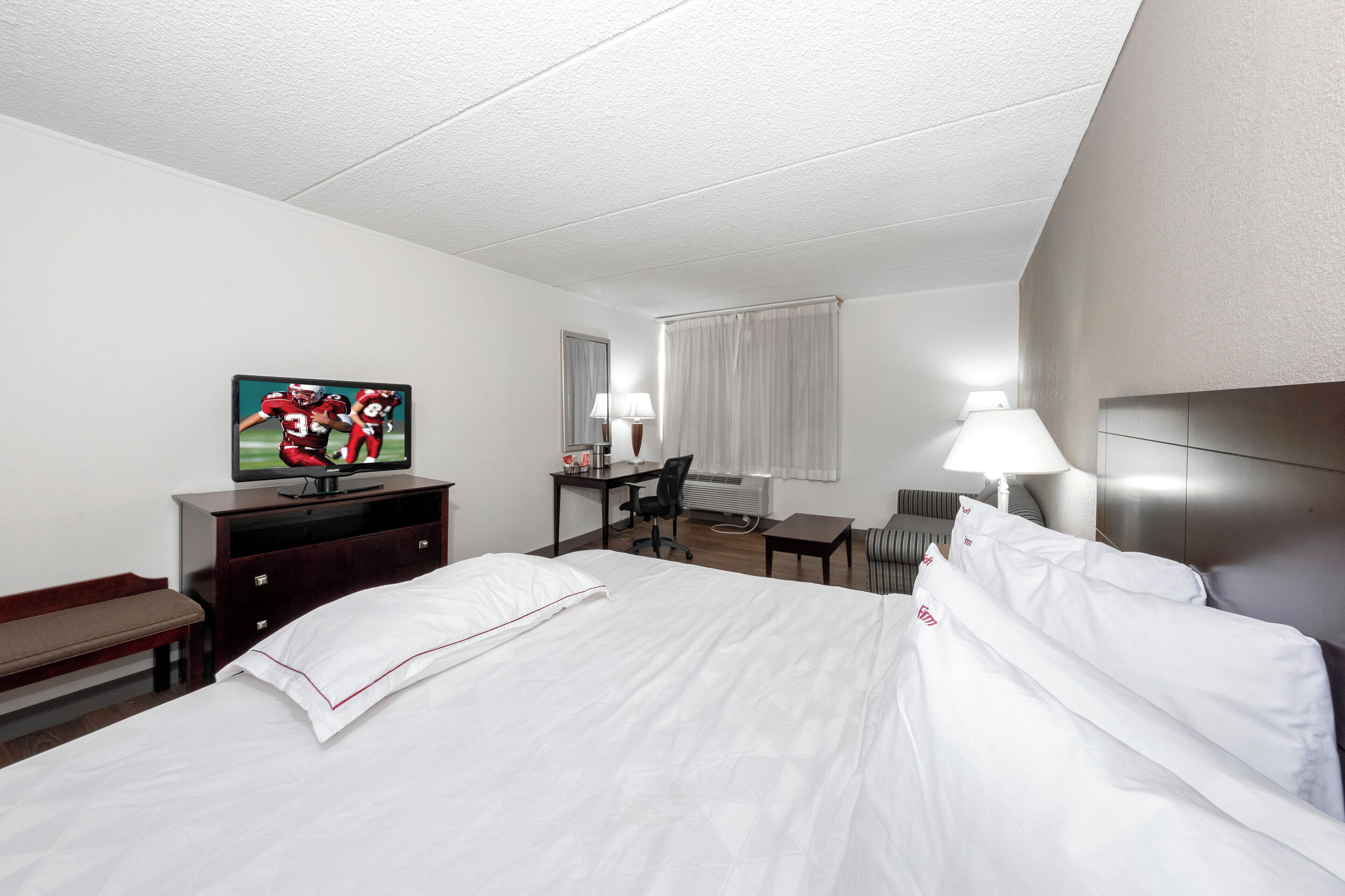 A hotel room with a bed, a desk, a chair, a television, and a window with curtains.