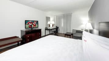 Une chambre d’hôtel avec un grand lit, un bureau avec une chaise, une télévision, une lampe et une fenêtre avec des rideaux.