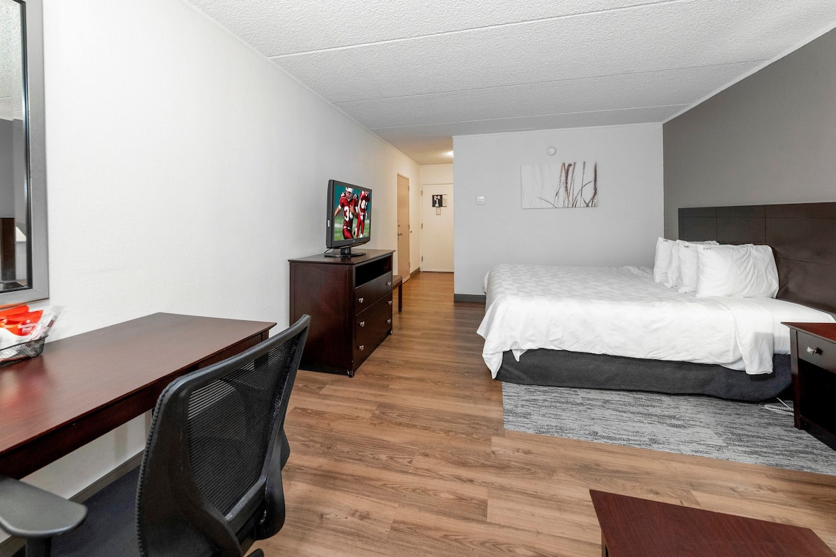 A hotel room with a bed, a desk with a chair, a television, and a dresser.