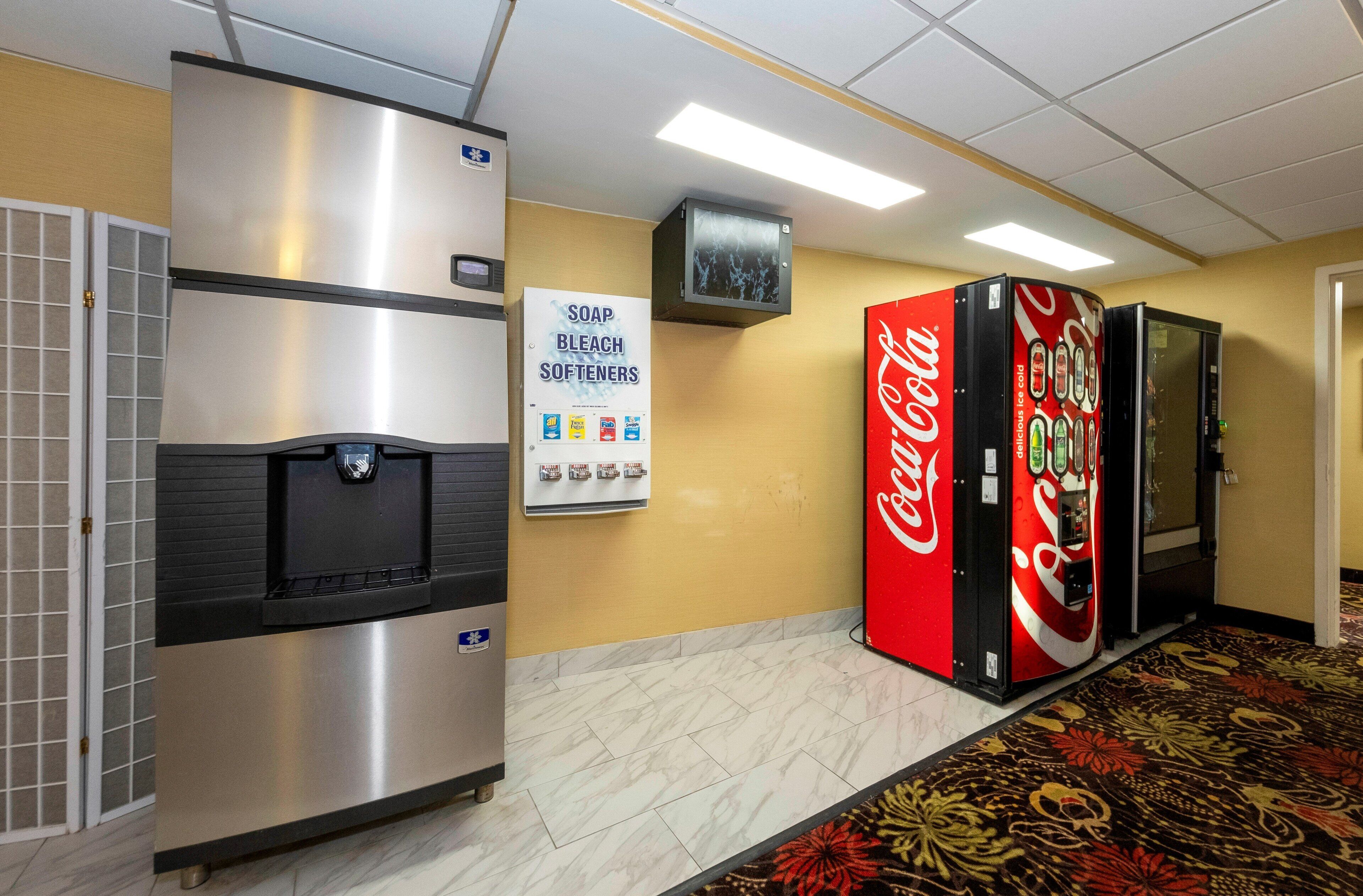 A hotel corridor with a refrigerator, a Coca-Cola vending machine, and a sign for soap, bleach, and softeners.