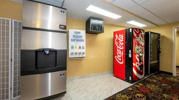 Pasillo de hotel con refrigerador, máquina expendedora de Coca-Cola y letrero indicando jabón, lejía y suavizantes.