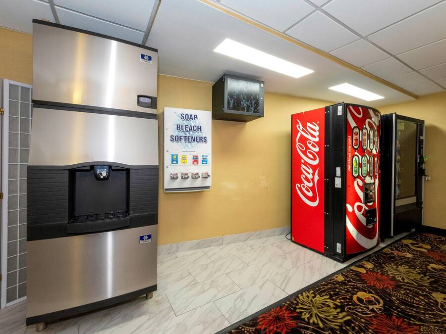 A hotel corridor with a refrigerator, a Coca-Cola vending machine, and a sign for soap, bleach, and softeners.