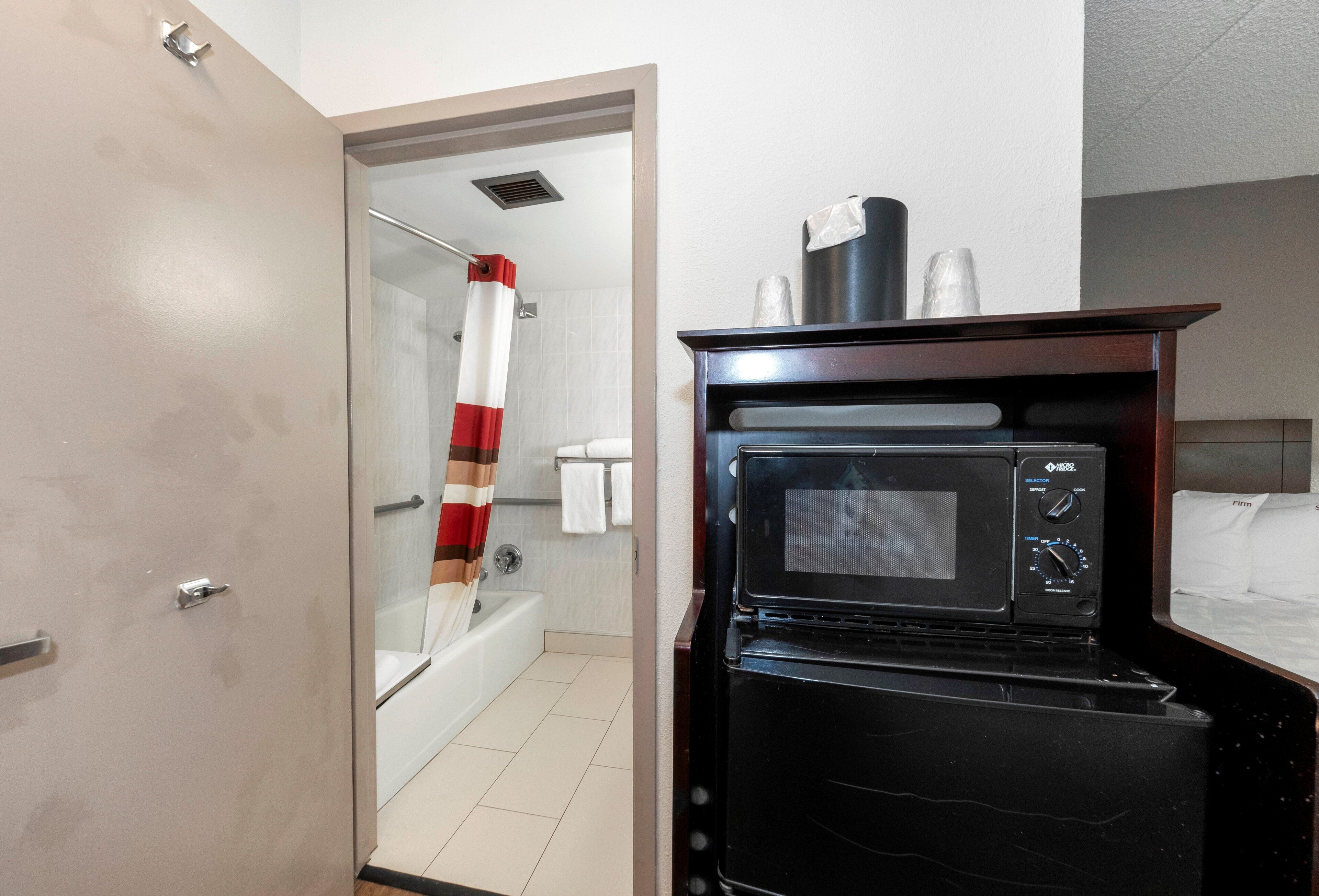 Ein kleines Hotelzimmer mit Dusche, Mikrowelle und einem Bett.