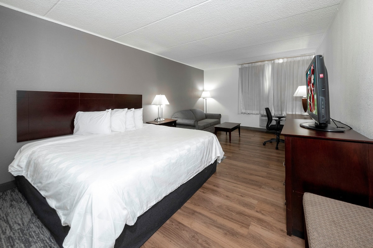 A hotel room with a large bed, two bedside tables with lamps, a desk with a computer, and a TV.