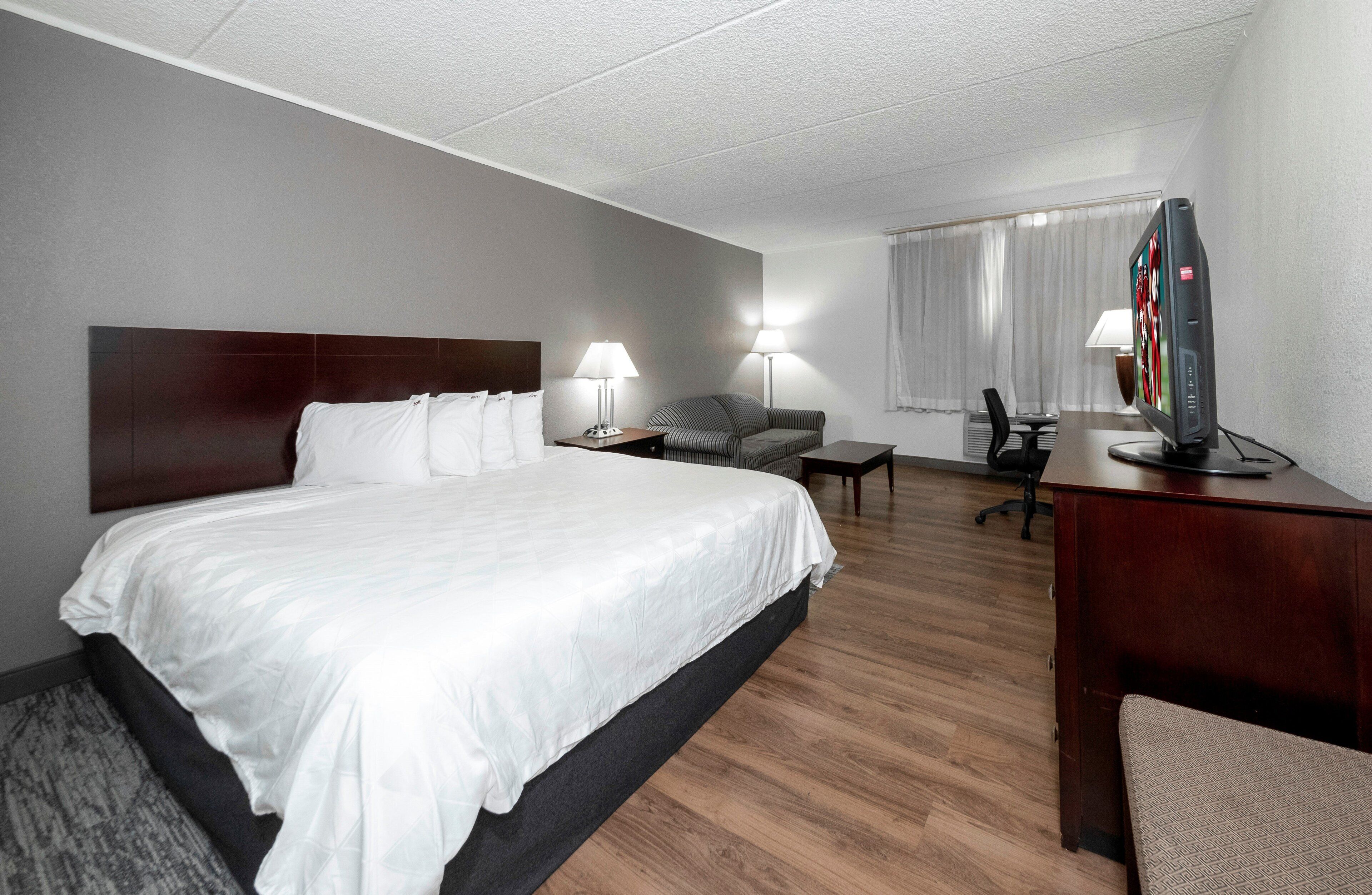 A hotel room with a large bed, a desk with a television, a chair, a lamp, and a window with curtains.