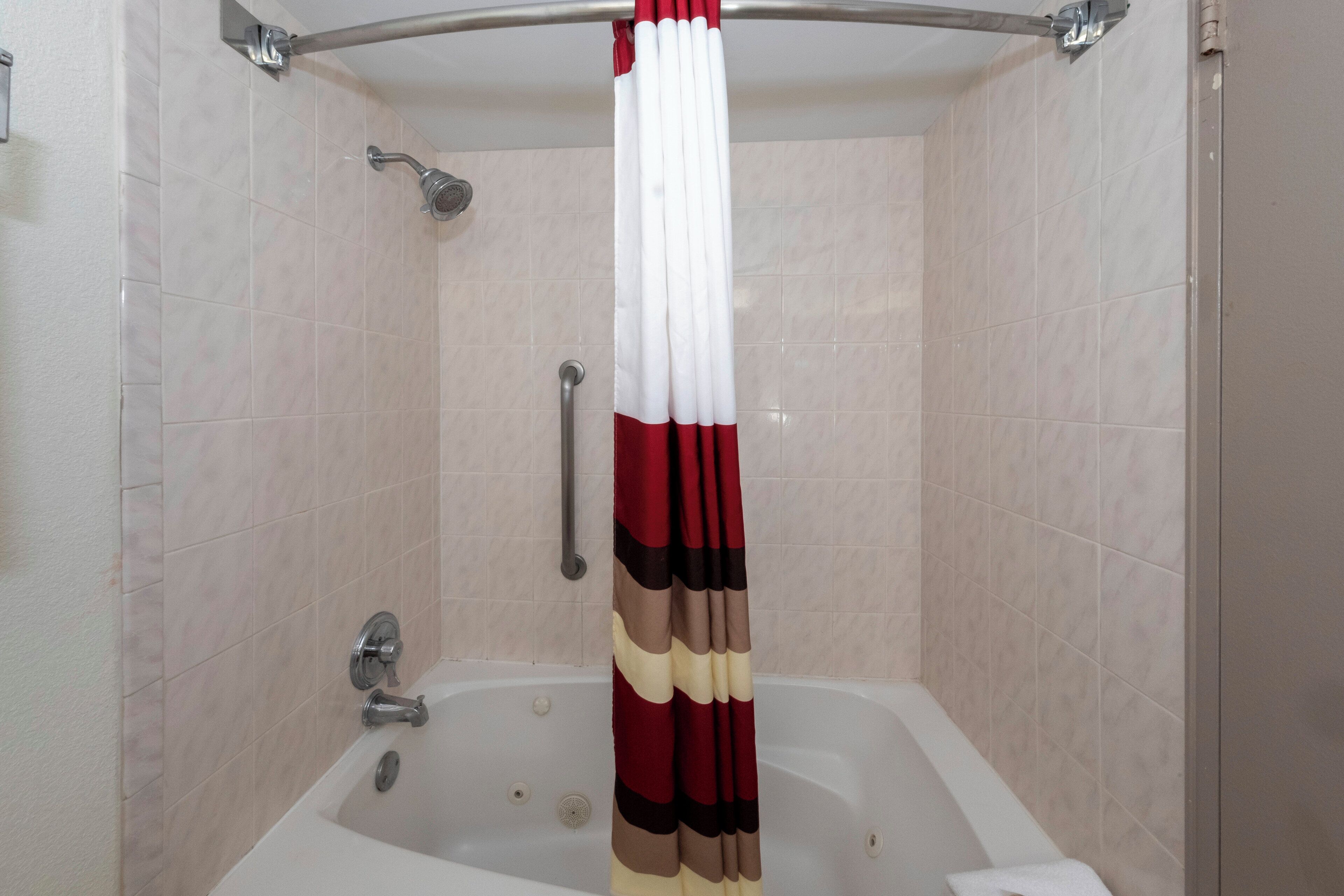 A bathroom with a bathtub, a shower, and a handrail.