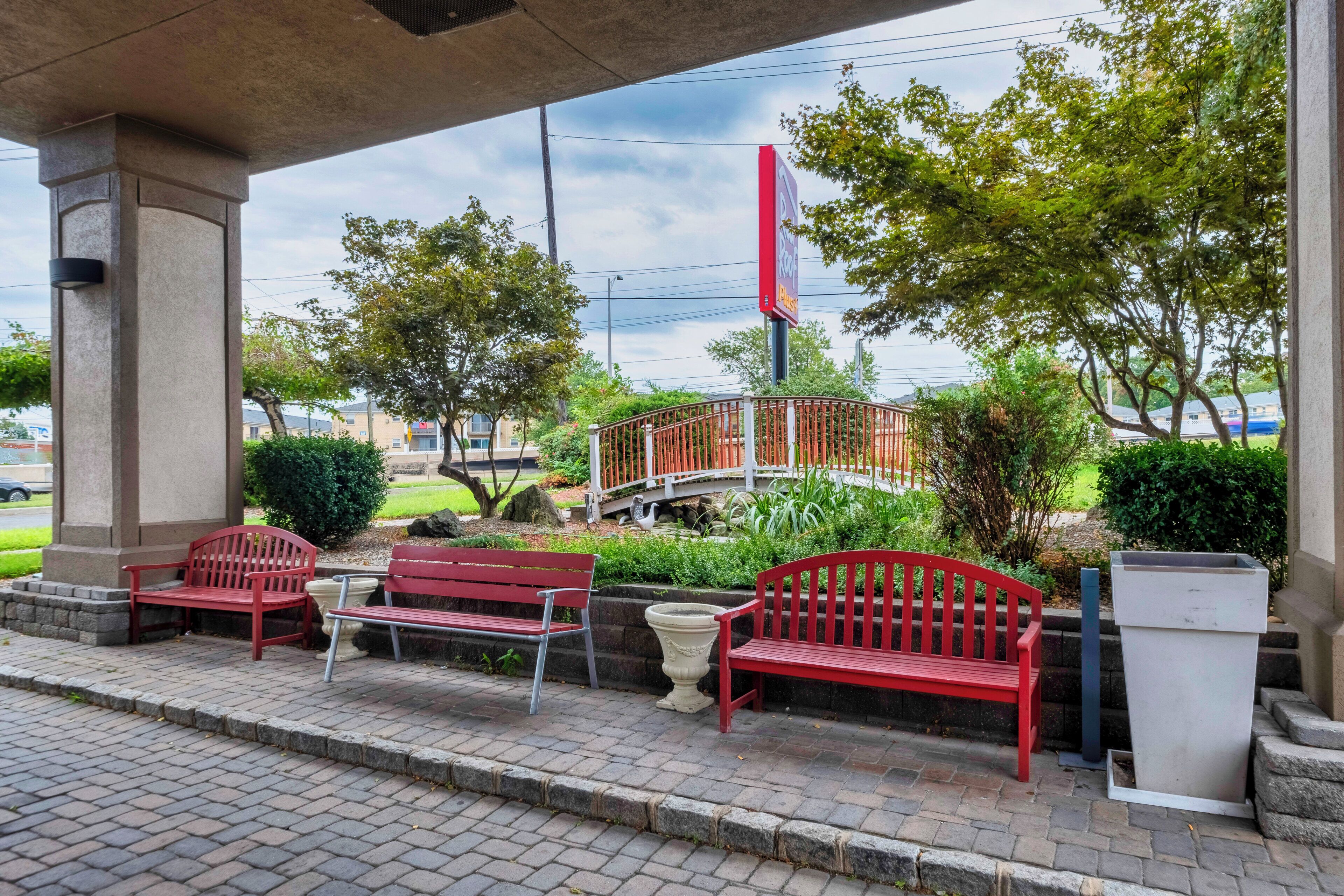 A covered outdoor seating area with red benches, a white trash bin, and a red sign.