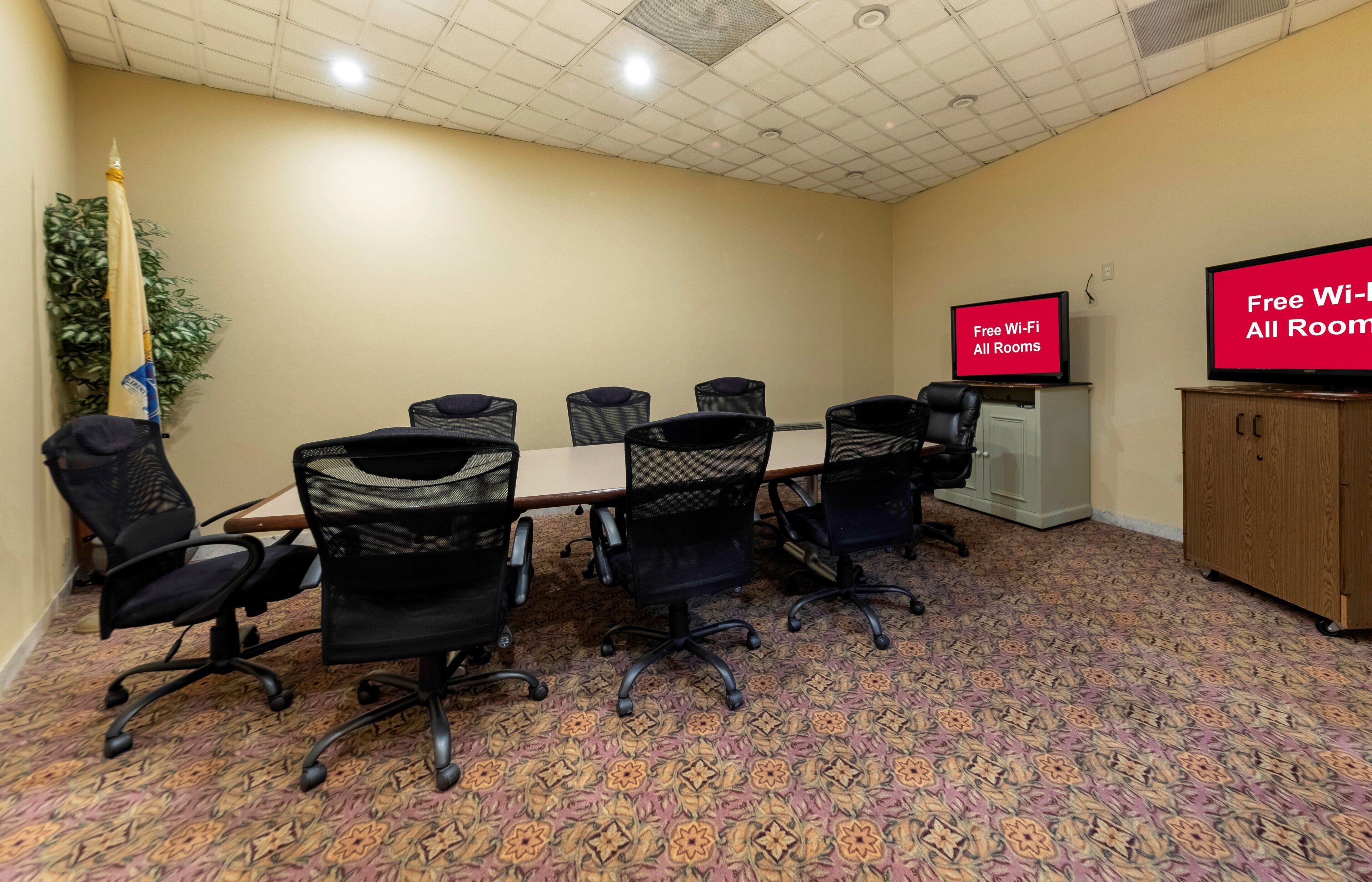 Une salle de conférence équipée d’une table, de chaises, d’un téléviseur affichant le message « Wi-Fi gratuit dans toutes les chambres » et d’un tapis à motifs.