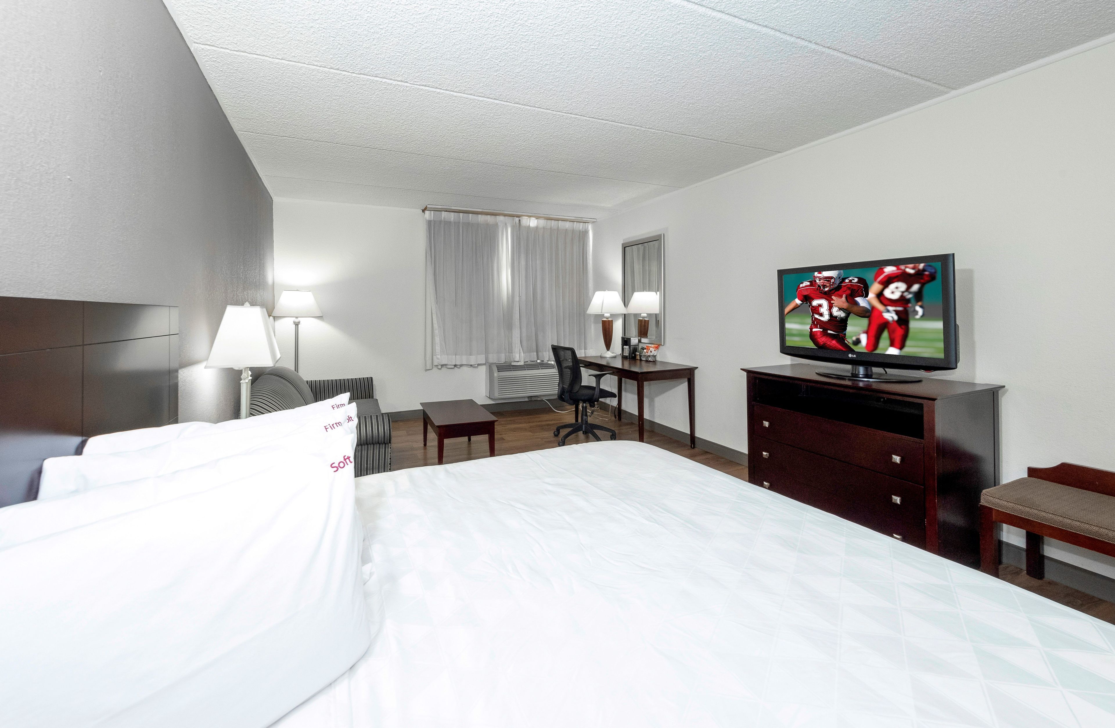 A hotel room with a bed, desk, chair, TV, and a small table.
