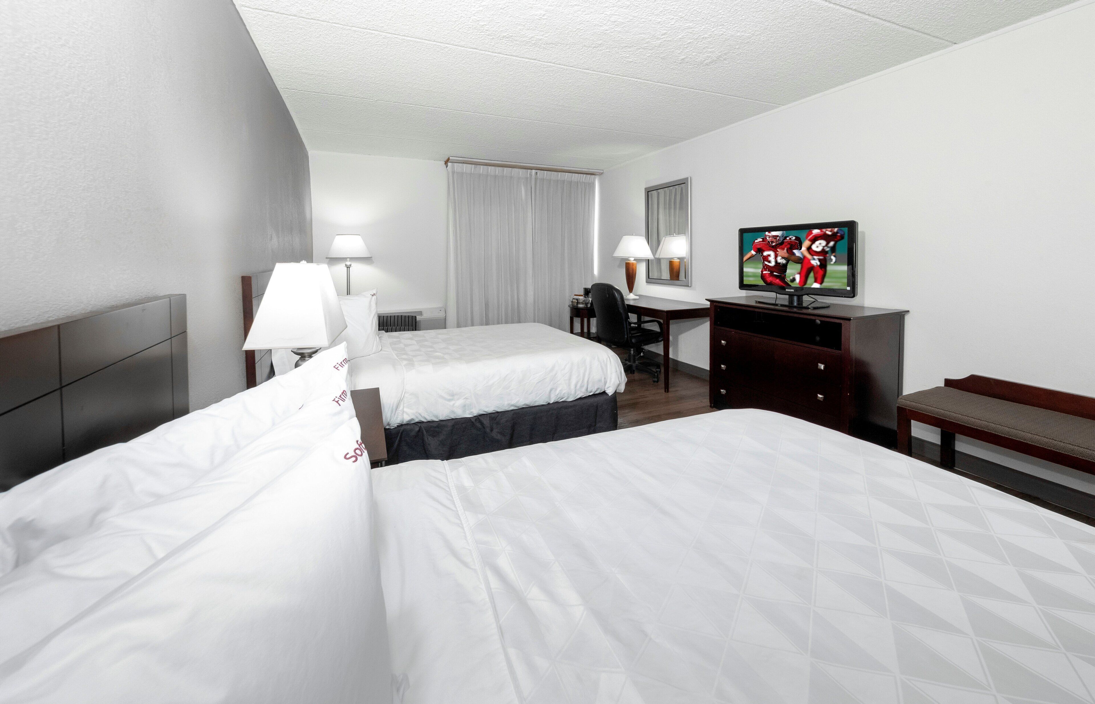 Quarto de hotel com duas camas, uma escrivaninha, televisão e um banco.