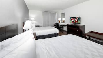 A hotel room with two beds, a desk, a television, and a bench.